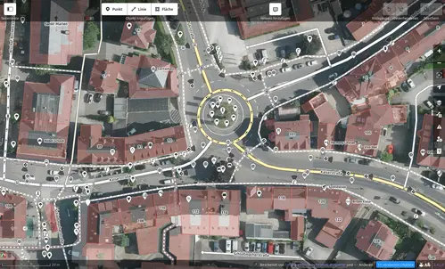 Das Foto zeigt die Bearbeitungsansicht der OpenStreetMap, ein Satellitenbild einer Kreuzung mit Kreisverkehr in Radevormwald. Eingefügte, weiße Linien zeigen den Verlauf der Straße. Zahlreiche, weiße Punkte im Bild symbolisieren Punkte wie Straßenlampen, zu denen weitere Details eingetragen sind.